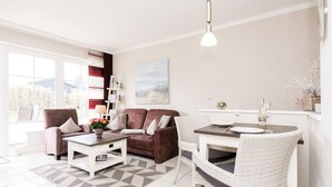 Ein modernes Wohnzimmer mit einem braunen Sofa, weißen Sessel, einem Couchtisch und einem Esstisch für zwei Personen.