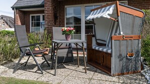 Ein Sitzbereich im Freien mit Korbstuhl, Tisch und gepolstertem Sitz einer Bank, mit Streifen-Markise.