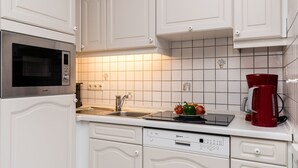 Eine moderne Küche mit weißen Schränken, einer Edelstahl-Mikrowelle, einer roten Kaffeemaschine und einem Geschirrspüler.