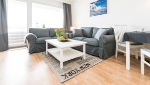 Ein modernes Wohnzimmer mit grauem Sofa, weißem Couchtisch und Meerblick durch große Fenster.