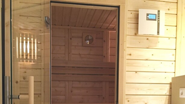 Un sauna doté d’une porte en verre, de lambris en bois, d’un panneau de commande et d’un évier.