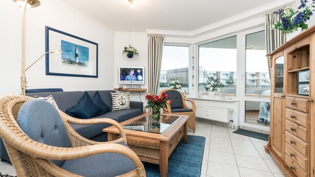 A modern living room with wicker furniture, a glass coffee table, and a view of the city through large windows. - Comfortable 2-room vacation apartment in the Nordmarkhof with balcony in Westerland (Westerland)