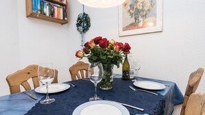 A dining table set with plates, cutlery, and wine glasses, surrounded by chairs. A vase with red roses is placed on the table. - Comfortable 2-room vacation apartment in the Nordmarkhof with balcony in Westerland (Westerland)