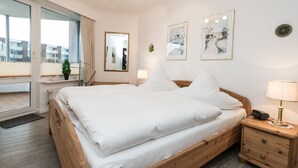 A bedroom with a large bed, wooden nightstands, a mirror, and artwork on the walls. - Comfortable 2-room vacation apartment in the Nordmarkhof with balcony in Westerland (Westerland)