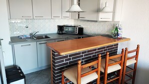 A kitchen with white cabinets, a brick backsplash, a wooden island with chairs, a microwave, and a hanging light fixture. - Comfortable vacation apartment with balcony in Westerland (Westerland)