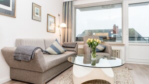 A modern living room with a sofa, a glass coffee table, and framed pictures on the wall. - Comfortable vacation apartment with balcony in Westerland (Westerland)