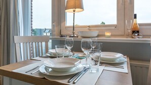 A dining table set with plates, cutlery, and glasses, a lamp, a candle, and a bottle of wine on a window sill. - Comfort. House 55 Grad Nord with balcony and modern furnishings in Wenningstedt (Wenningstedt)