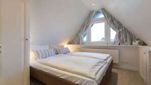 A bedroom with a large bed, a window with curtains, a radiator, and a white wardrobe. - Comfort. House 55 Grad Nord with balcony and modern furnishings in Wenningstedt (Wenningstedt)