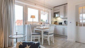 A modern kitchen with white cabinets, a dining table, and a small round table with a lamp. - Comfort. House 55 Grad Nord with balcony and modern furnishings in Wenningstedt (Wenningstedt)