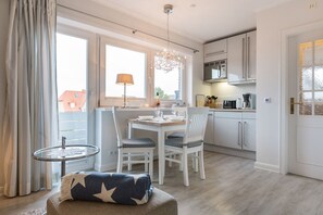 A modern kitchen with white cabinets, a dining table, and a small round table with a lamp. - Comfort. House 55 Grad Nord with balcony and modern furnishings in Wenningstedt (Wenningstedt)
