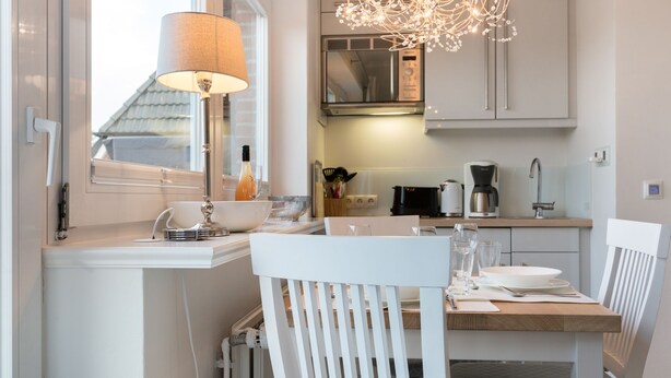 A modern kitchen with white cabinetry, a dining table, chairs, a lamp, and a chandelier. - Comfort. House 55 Grad Nord with balcony and modern furnishings in Wenningstedt (Wenningstedt)