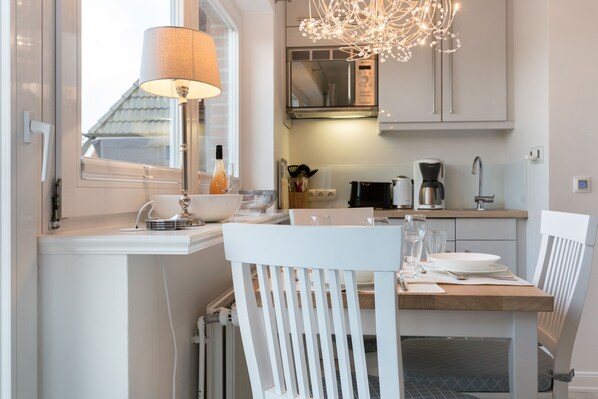 A modern kitchen with white cabinetry, a dining table, chairs, a lamp, and a chandelier. - Comfort. House 55 Grad Nord with balcony and modern furnishings in Wenningstedt (Wenningstedt)
