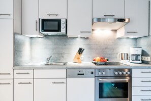 Une cuisine moderne avec des meubles blancs, un four à micro-ondes encastré, une machine à café et un four.