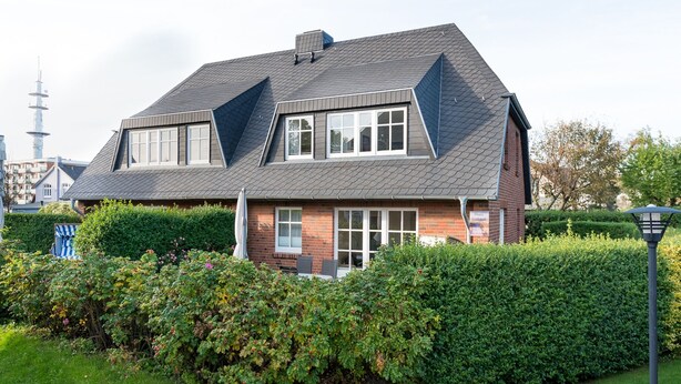 Ett tvåvåningshus med ett sluttande tak, en fasad av tegel och en välskött trädgård med häckar och en gräsmatta.