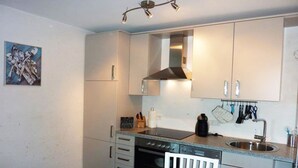 A compact kitchen with a stove, oven, and sink. There is a white chair and a black table. - Modern vacation apartment with sauna, solarium and heated indoor pool in Westerland (Westerland)