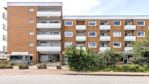 A multi-story residential building with balconies, a ground-level entrance, and a small commercial space on the ground floor. - Modern vacation apartment with sauna, solarium and heated indoor pool in Westerland (Westerland)