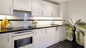 A modern kitchen with white cabinets, a black countertop, and a built-in oven. - Hertford Flat 12 (London)