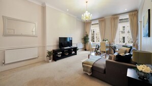 A living room with a sofa, TV, and a chandelier. - Hertford Flat 12 (London)
