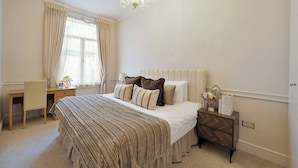 A bedroom with a large bed, a desk, and a nightstand. - Hertford Flat 12 (London)