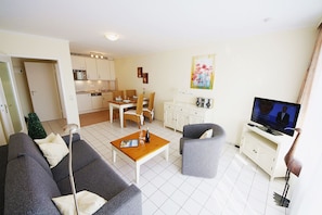 A living room with a sofa, a coffee table, a television, and a dining area with chairs and a table. - Modern vacation apartment with sauna and heated indoor pool in Westerland (Westerland)