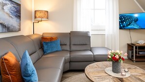 En moderne stue med en hjørnesofa, et rundt sofabord med en vase blomster, et fladskærms-tv og en lampe.