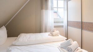 Et hotelværelse med to senge, hvidt sengetøj, et stort vindue med udsigt og en rumdeler med vævet mønster.