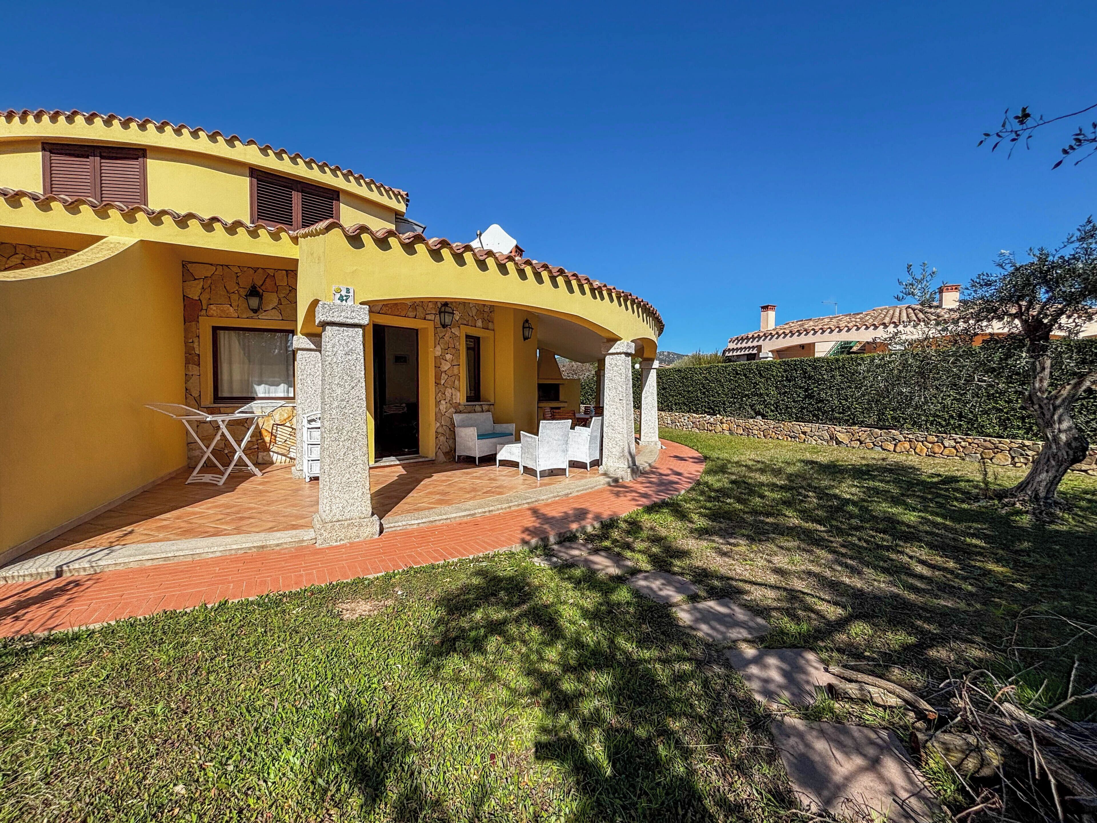 A yellow villa with a stone facade, outdoor seating area, and a stone wall surrounding the property.