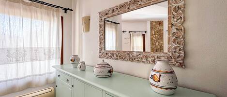 A bathroom with a light green vanity, a decorative mirror with an ornate frame, and a window with sheer curtains.