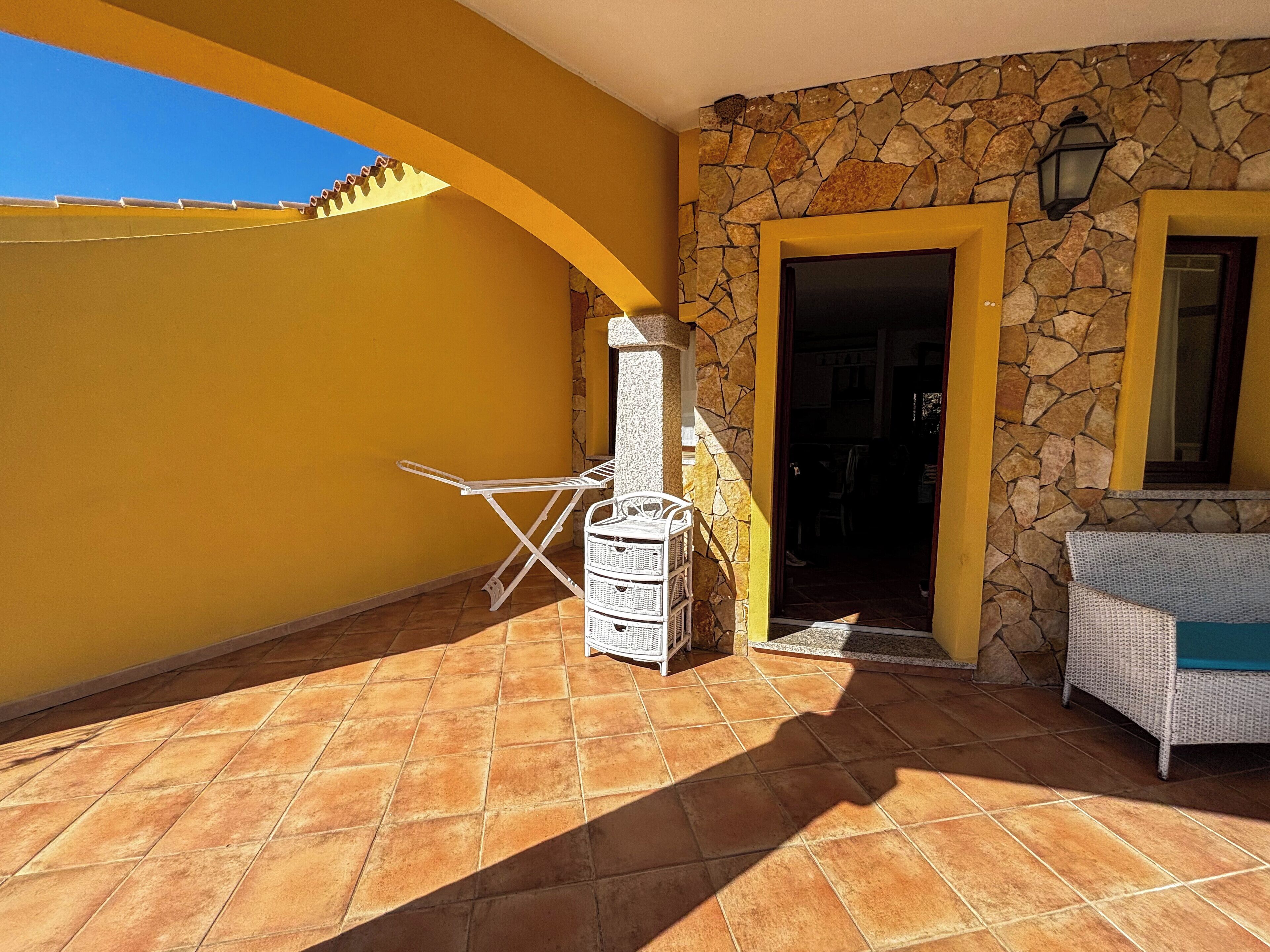 Un patio con un muro de piedra, una silla plegable blanca y una pequeña mesa.