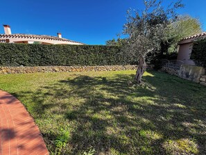 A well-maintained garden with a stone wall, a tree, and a brick pathway. - Villa Sa Fina (Costa Rei)