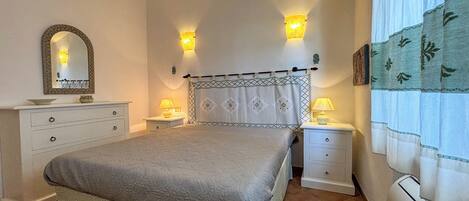 A bedroom with a bed, two bedside tables, a nightstand, a dresser, a mirror, and a window with curtains.