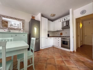 A compact kitchen with white cabinets, a built-in oven, and a tiled floor. - Villa Sa Fina (Costa Rei)