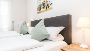 Ein ordentlich bezogenes Bett mit weißen Laken und zwei Kissen, ein Nachttisch aus Holz mit einer Lampe und ein Gemälde an der Wand.