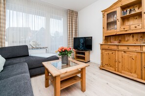 A modern living room with a sofa, a glass-top coffee table, a wooden cabinet, and a television. - Modern vacation apartment with sauna and heated indoor pool in Westerland (Westerland)