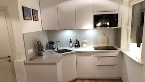 A modern kitchen with white cabinets, a built-in microwave, and a sink. There are two framed pictures on the wall, a wine bottle, and a glass on the counter. - Exclusive vacation apartment with a view of the sea (Wenningstedt)