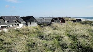 A coastal building complex with multiple houses, some with sloped roofs, and a view of the sea in the background. - Exclusive vacation apartment with a view of the sea (Wenningstedt)