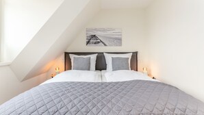 A neatly made bed with a grey quilt, two bedside lamps, and a framed picture on the wall. - This beautiful and new terraced house is centrally located in Westerland (Westerland)
