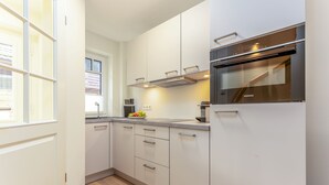 A modern kitchen with white cabinetry, a built-in oven, and a window providing natural light. - This beautiful and new terraced house is centrally located in Westerland (Westerland)