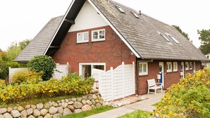 A two-story brick house with a sloped roof, a white exterior, and a small porch with a chair. - Comfortable vacation apartment with terrace and garden in Wenningstedt (Wenningstedt)