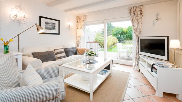 A modern living room with a white sofa, a coffee table, a flat-screen TV, and a large window with curtains. - Comfortable vacation apartment with terrace and garden in Wenningstedt (Wenningstedt)