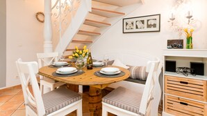 A dining area with a round wooden table, white chairs, and a bench. A staircase with white railings is visible in the background. - Comfortable vacation apartment with terrace and garden in Wenningstedt (Wenningstedt)