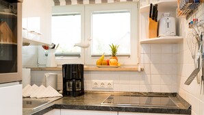 A modern kitchen with white cabinets, a black countertop, a coffee maker, and a fruit bowl on the windowsill. - Comfortable vacation apartment with terrace and garden in Wenningstedt (Wenningstedt)