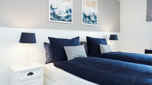 Ein Doppelbett mit dunkelblau bezogener Bettwäsche, einem weißen Kopfteil und passenden Nachttischen mit Lampen.