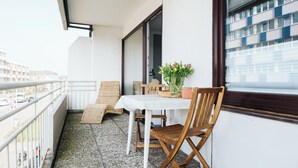 Ein Balkon mit Tisch, Stühlen, einer Blumenvase und Blick auf Gebäude.
