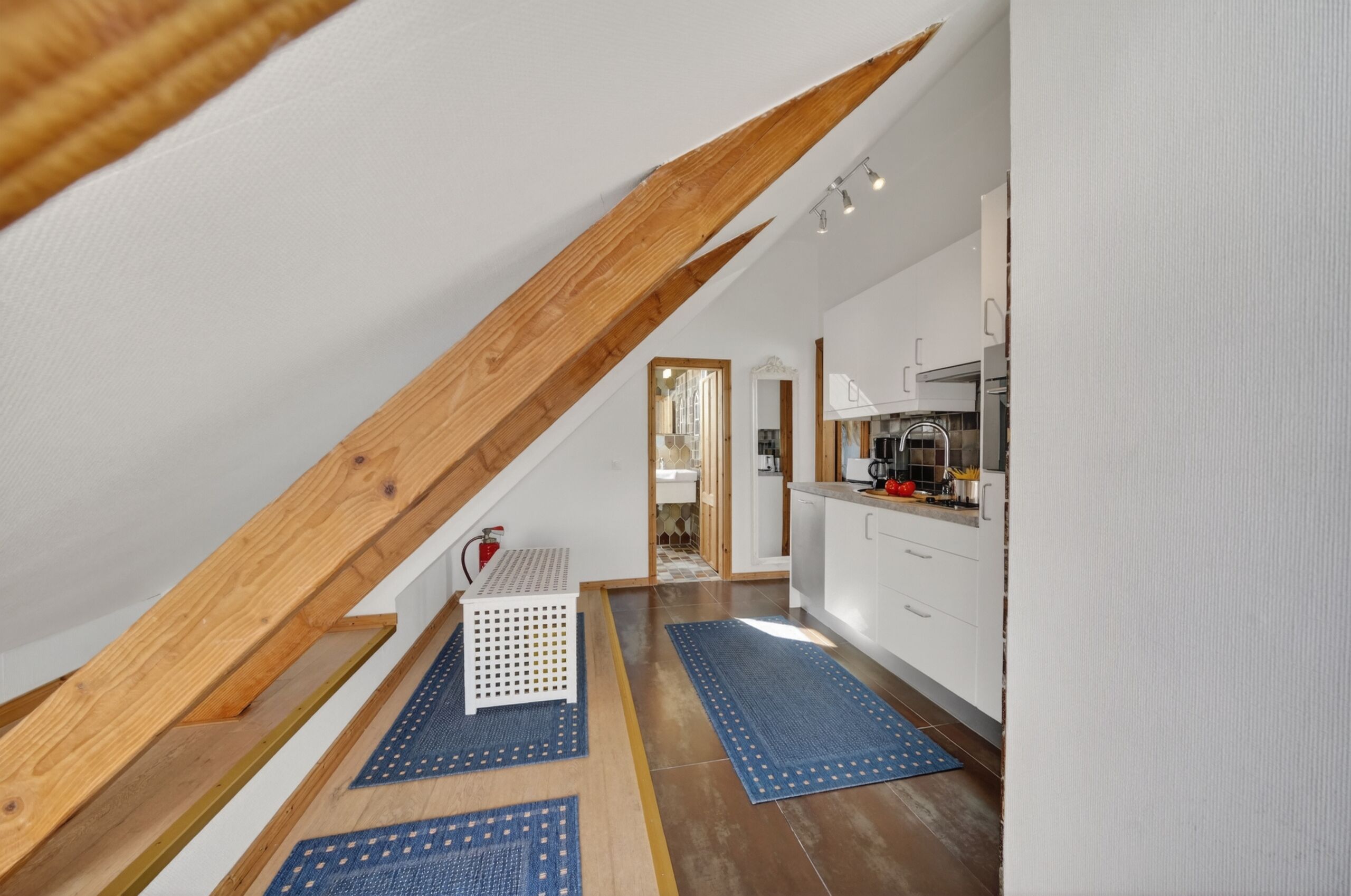 A modern kitchen with white cabinets, a wooden ceiling, and a small seating area with a white chair and a blue rug.