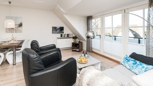 Una sala de estar moderna con un sofá, una mesa de centro con frutas, un comedor con mesa y sillas, y una cocina con un refrigerador y un lavamanos.