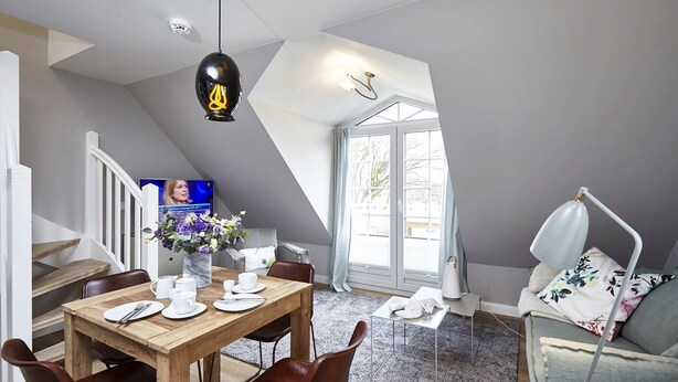 Een eetruimte met een houten tafel voor vier personen, een vaas met bloemen en een moderne hanglamp.