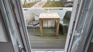 Een open schuifdeur naar een balkon met een houten tafel en twee stoelen.
