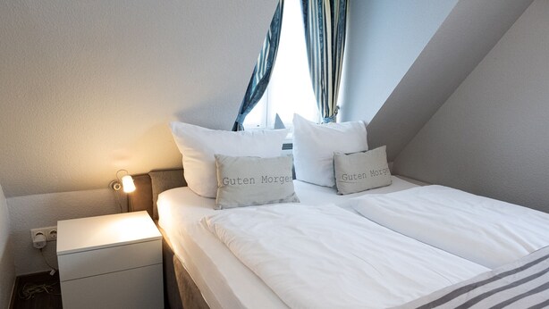 Una cama bien tendida con ropa de cama y almohadas blancas con la inscripción 'Guten Morgen'.