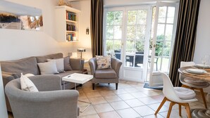 Una sala de estar con un sofá, sillones, una mesa de centro, una estantería y un comedor con una mesa y sillas.